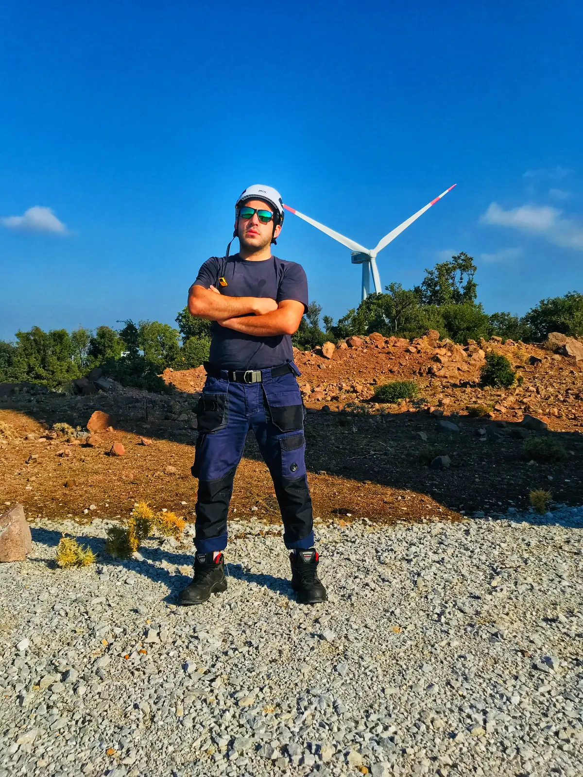 Baret ve iş kıyafetiyle türbinin önünde duran teknisyen